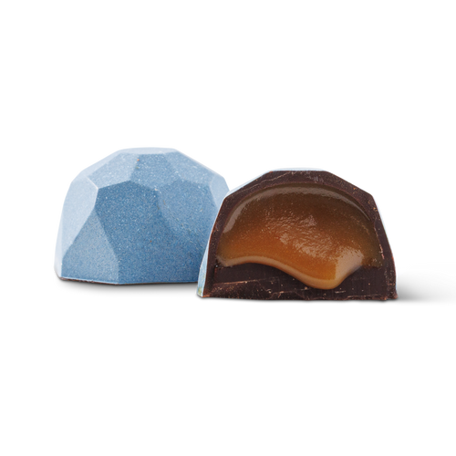 Two faceted gourmet chocolates on a white background, with one whole chocolate in light blue and one cut open showing a caramel-colored filling.